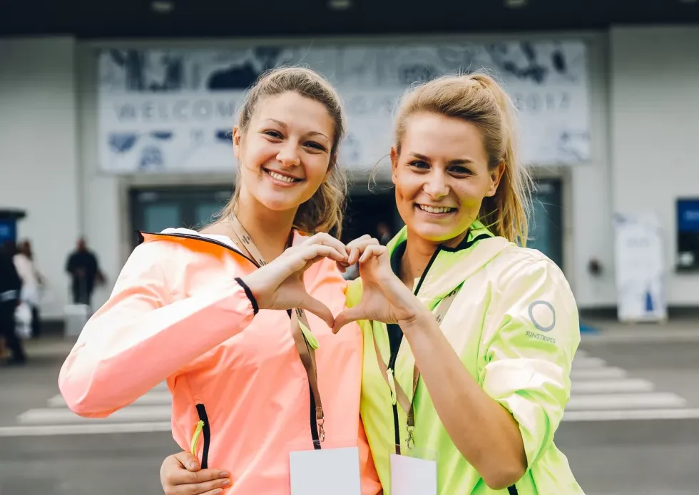 Zwei Frauen auf einer Messe formen ihre Hände gemeinsam zu einem Herzen